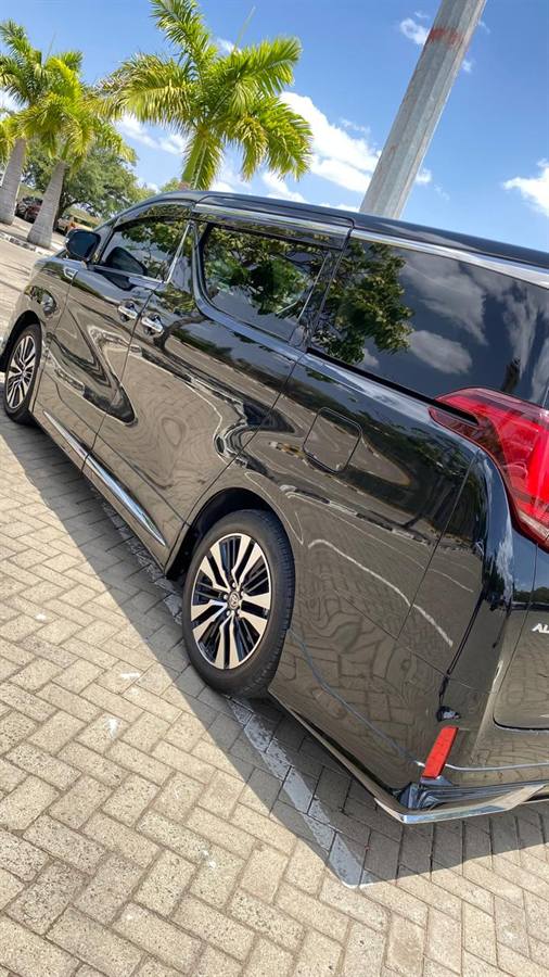 A black Toyota Alphard van parked on herringbone paving beside palm trees