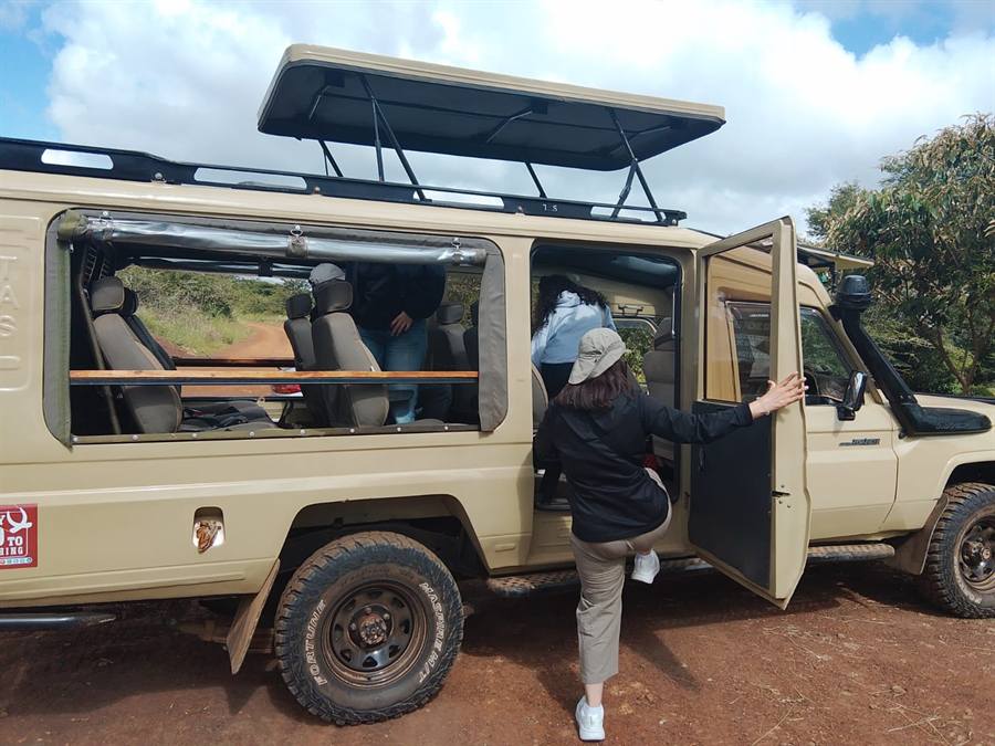 A cream Land Cruiser 4x4 safari vehicle with its pop-up roof raised and a guest stepping in through the open door