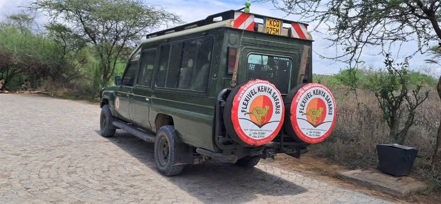 The back of a dark green 4x4 safari vehicle with two Flexivel Kenya Safaris wheel covers on cobbled paving