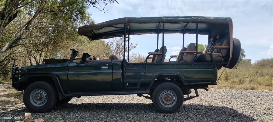 Side view of a dark green open-sided Land Cruiser game viewer with a canopy roof and rows of seats