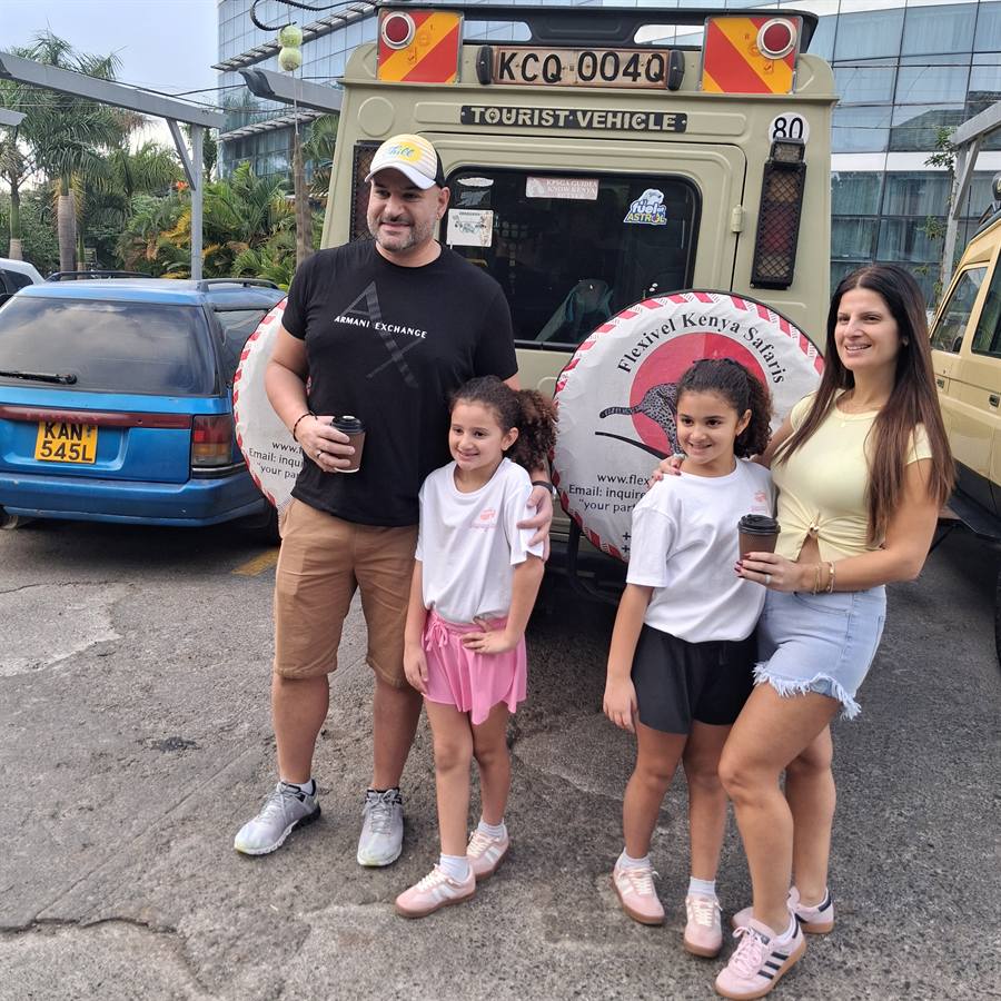 A family posing behind a Flexivel Kenya Safaris safari vehicle with its logo wheel cover