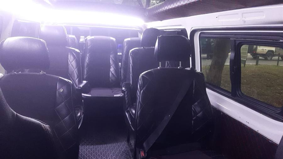 The inside of a safari van with rows of black leather seats and large windows