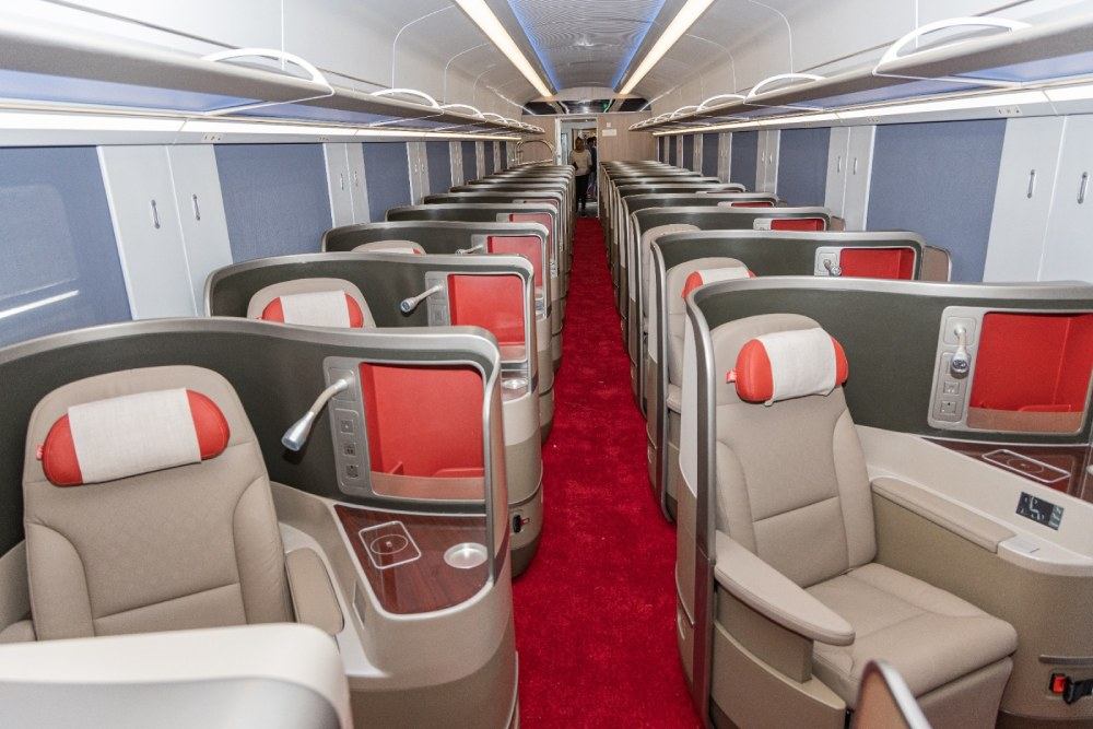 The inside of an SGR first class carriage with rows of reclining seats with red headrests and a red carpet